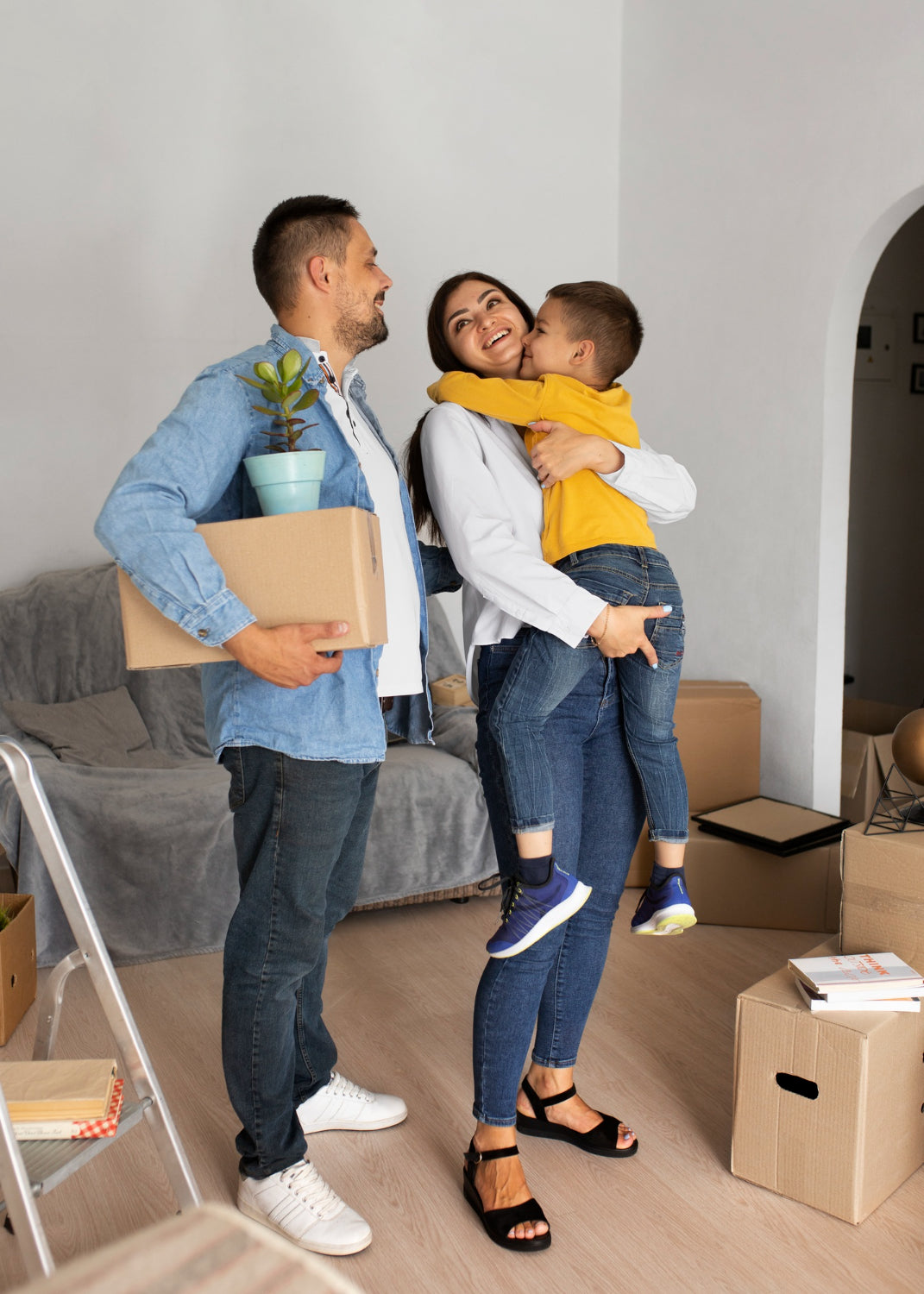 Family of three in a new home with moving boxes and a plant.